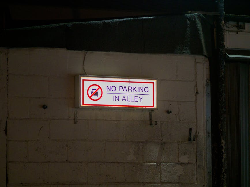 Close-up of a round traffic sign with a red border and a white background, featuring a black pictogram of a person standing next to a car, indicating a parking or stopping restriction for vehicles. Th
