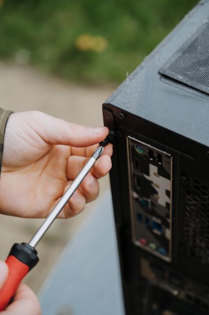 Close-up view of a person’s hand, clad in a dark jacket, placing four AA alkaline batteries into a green recycling bin specifically designated for used batteries, with a red flame symbol and German